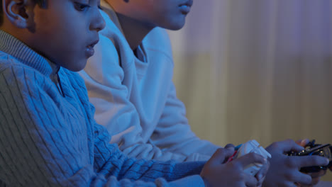 Primer-Plano-De-Dos-Niños-Pequeños-En-Casa-Jugando-Con-Una-Consola-De-Juegos-De-Computadora-En-La-Televisión-Sosteniendo-Controladores-A-Altas-Horas-De-La-Noche